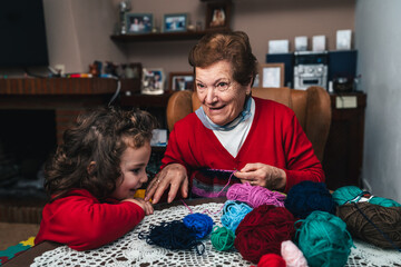 horizontal photo of grandmother and grandson having fun while sewing with a needle in the living...