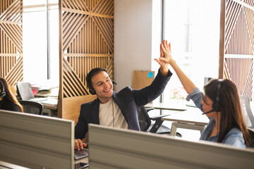 Call center representatives wearing headsets and celebrating a sale with a high five