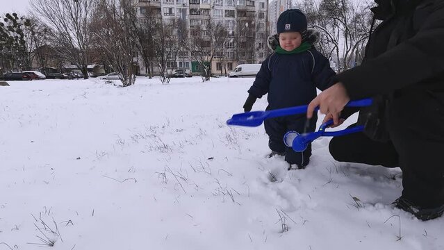 Father and son make snowballs and throw snow with a shovel. Ideas about winter, cold, emotions, nature, childhood, fun, family holidays, laughter, games, affection, trust, environmental exploration
