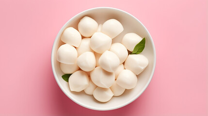 Mozzarella cheese balls in bowl on light pink background, top view	