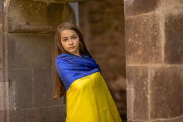 Girl in Ukrainian flag looking afar standing by an ancient wall