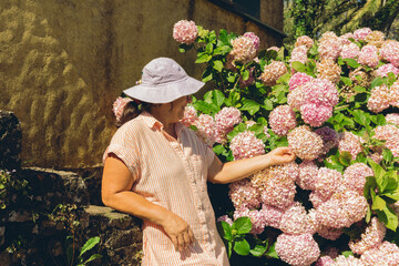 middle-aged Latin woman contemplating pink flower Hydrangea macrophylla in her garden