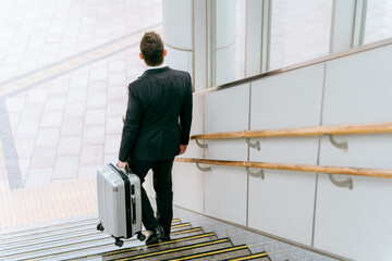 スーツケースを持って階段を降りる外国人ビジネスマン
 - obrazy, fototapety, plakaty