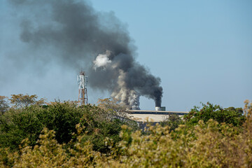 Industrial factories with pipes emit white and black smoke into the sky, which pollutes the environment and destroys the ecosystem.