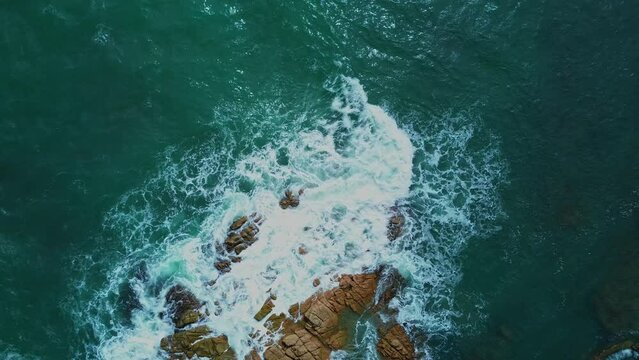 Aerial shot looking down at a seascape with waves crashing against the rocks on a small island. Sea nature background, travel.