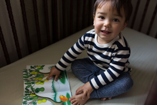 Toddler reading a story book in a crib