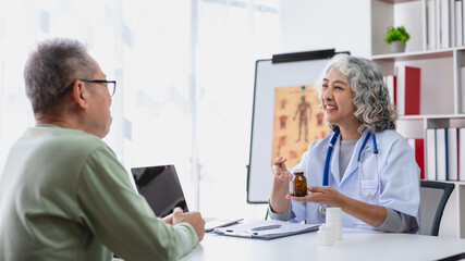 Mature asian doctor explaining prescription medication to an attentive senior male patient during a...