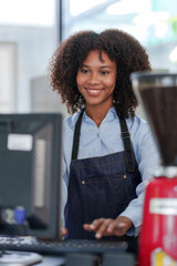 Smiling young barista in apron using cash register at modern cafe. - obrazy, fototapety, plakaty