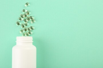 Bottle and vitamin capsules on turquoise background, top view. Space for text