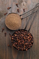Aromatic clove powder and dried buds in scoops on wooden table, top view