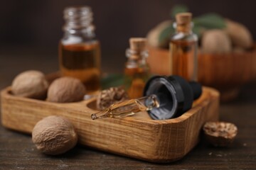 Obraz na płótnie Canvas Nutmeg essential oil and nuts on wooden table, closeup