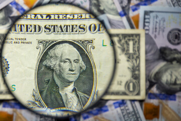 One American dollar note with George Washington face portrait magnified with a magnifying glass, on a background of notes of various denominations. Monetary wallpaper.