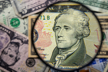 10 American dollar note with Alexander Hamilton face portrait magnified with a magnifying glass, on a background of notes of various denominations. Monetary wallpaper.