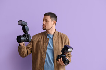 Male photographer with professional cameras on lilac background