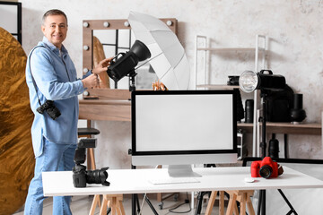 Mature photographer with lighting equipment and computer in studio - Powered by Adobe