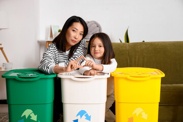 Asian mother with her little daughter and recycle bins at home