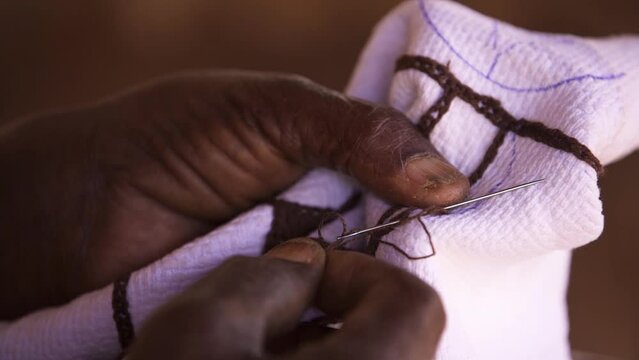 A man embroiders traditional African clothing with a needle.