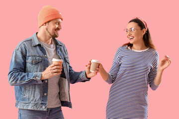 Happy young couple with cups of coffee on pink background