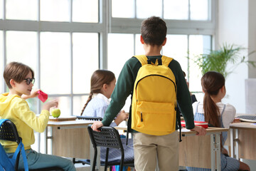 Little boy with backpack in classroom, back view - obrazy, fototapety, plakaty