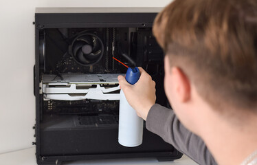 Young man cleaning the inside of a computer with compressed air duster