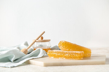 Board with fresh honeycombs and dipper on light background
