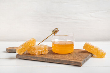 Kitchen board with jar of sweet honey and combs on light wooden table