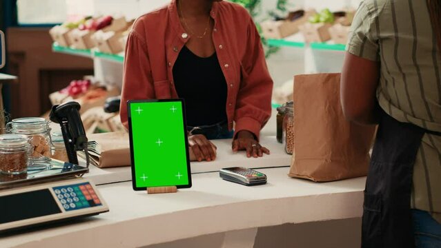 Tablet showing isolated greenscreen display at cash register, running blank chromakey template in local farmers market. Vendor having gadget with copyspace mockup layout in supermarket.