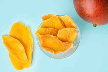 Glass bowl with slices of dried mango on blue background
