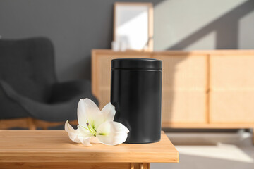 Mortuary urn and white lily flower on wooden table in room