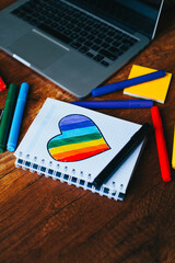 Photograph of notebook on wooden table with hand drawn LGBTQ+ heart. Concept of people and...