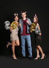 Fototapeta na wymiar Young friends with champagne and figure 2024 on dark background. New Year celebration