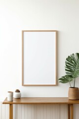 Minimalist frame mockup resting on a wooden table, next to a lovely plant, isolated white wall with sunlight at background...