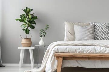 Grey bedroom with a wooden bench patterned pillows on bed and a plant on a white nightstand - Powered by Adobe