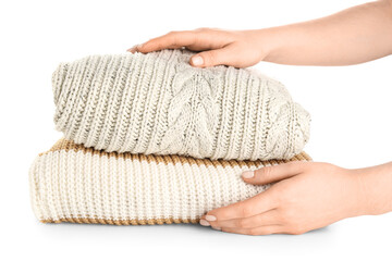 Female hands with stack of different stylish sweaters on white background