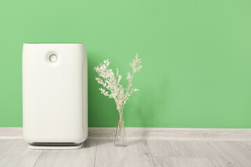 Air purifier and vase with plant branches near green wall in room