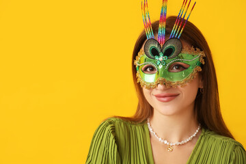 Beautiful young woman in carnival mask on yellow background