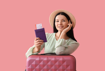 Beautiful young woman with passport, ticket and suitcase on pink background