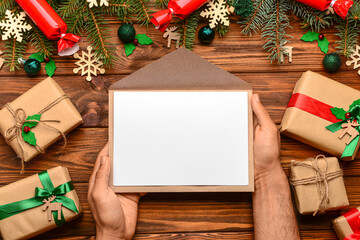 Man holding envelope with blank paper, Christmas decor and gifts on wooden background. Letter to Santa