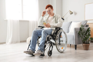 Young man in wheelchair using mobile phone at home