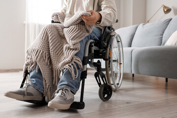 Young man in wheelchair with plaid at home - obrazy, fototapety, plakaty