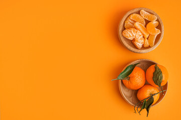 Wooden bowls with tasty tangerines, segments and leaves on orange background