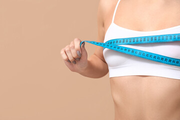 Young woman measuring her breast on brown background
