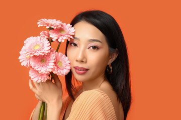 Fototapeta premium Beautiful young Asian woman with bouquet of pink gerbera flowers on orange background
