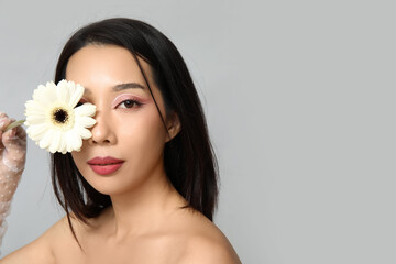 Beautiful young Asian woman with white gerbera flower on grey background