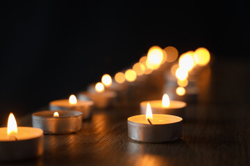 Burning candles on wooden shelf against black background, closeup. International Holocaust Remembrance Day - obrazy, fototapety, plakaty