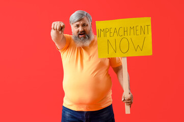 Protesting mature man holding placard with text IMPEACHMENT NOW and pointing at something on red...