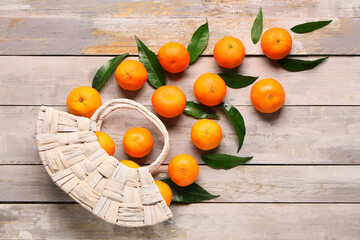 Wicker bag with sweet mandarins and leaves on grey wooden background