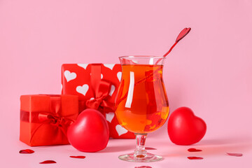 Glass of tasty cocktail with hearts and presents on pink background, closeup. Valentine's Day celebration