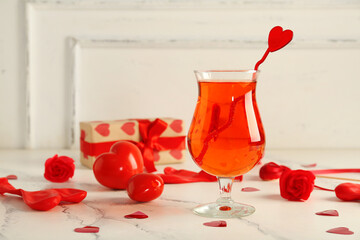 Glass of tasty cocktail with hearts and roses on light table, closeup. Valentine's Day celebration