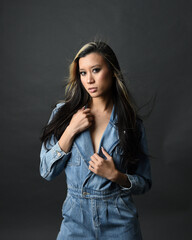 close up portrait of brunette female asian model wearing casual clothes, double denim jean outfit. Isolated on dark studio background with shadows. strong fashion model posing.